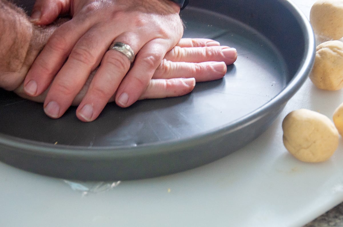 Two hands pressing down on a heavy dish for the purpose of flattening a tortilla.