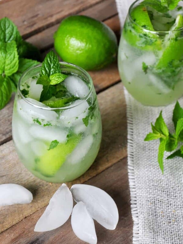 Mojito on a picnic table with mint, ice, and a whole lime.