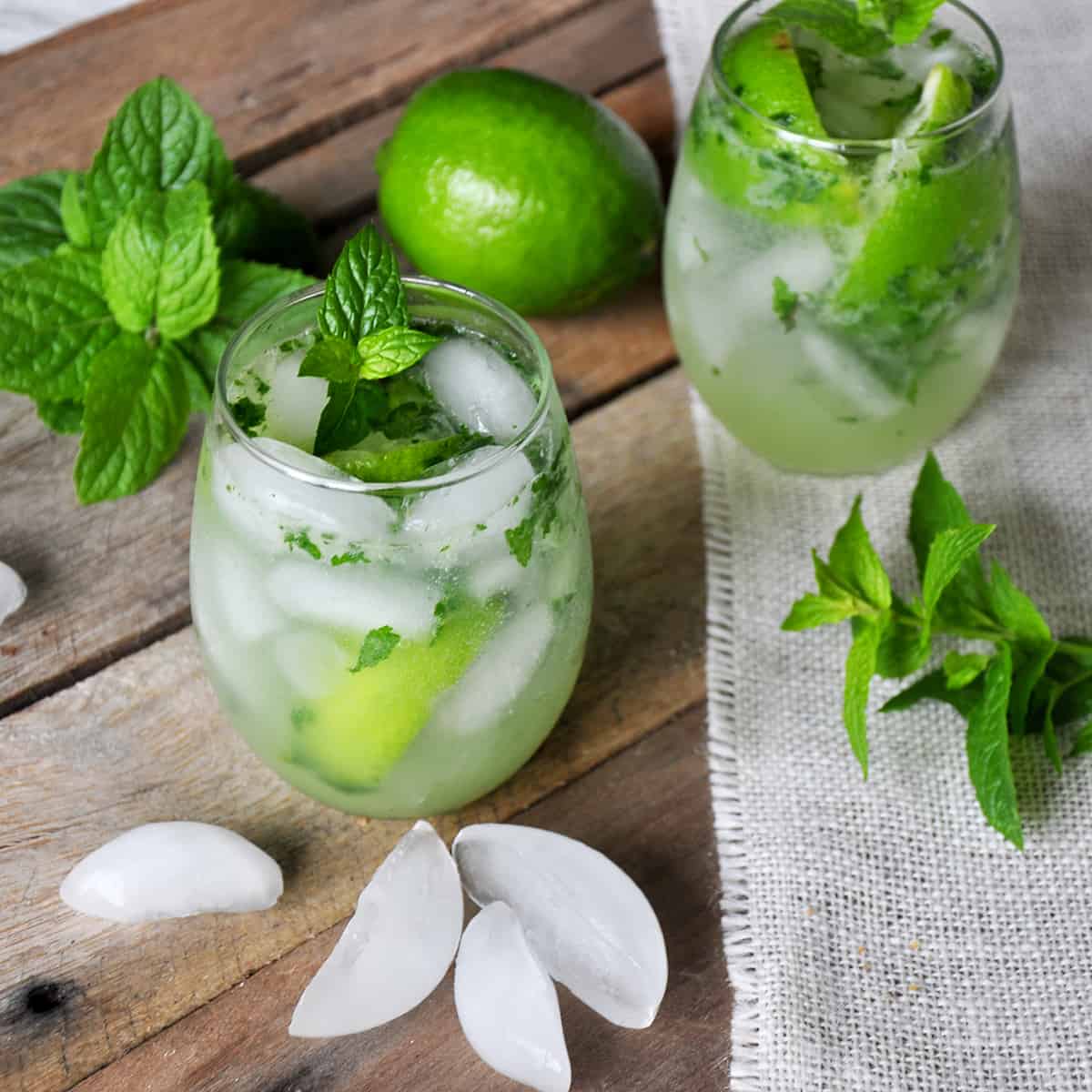 Mojito on a picnic table with mint, ice, and a whole lime.