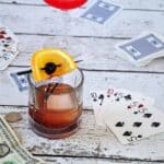 A picture of a mad men old fashioned on a park table with cards in the background