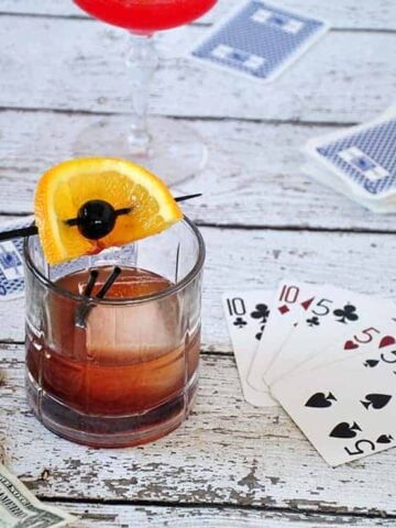 A picture of a mad men old fashioned on a park table with cards in the background