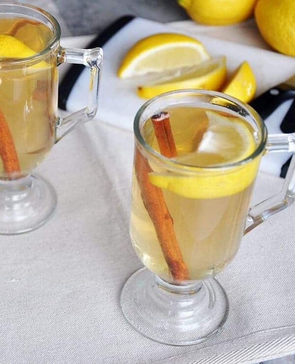 best hot toddy recipe. Hot toddy on a table with lemon, cinnamon, and a cutting board.