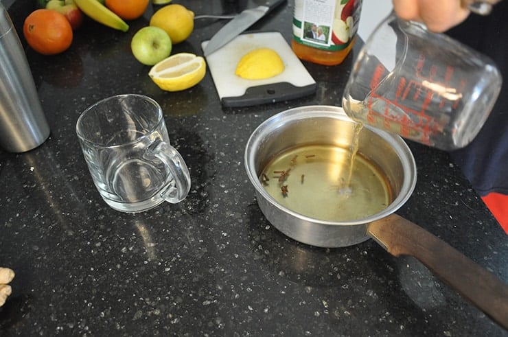 Getting Apple Ginger Hot toddy ingredients put together. Pouring cider into pot with fruit in background