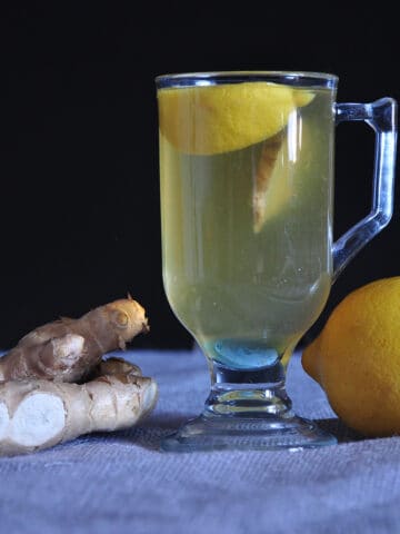 Hot toddy for a cold pictured with a lemon and ginger on a tablecloth covered counter