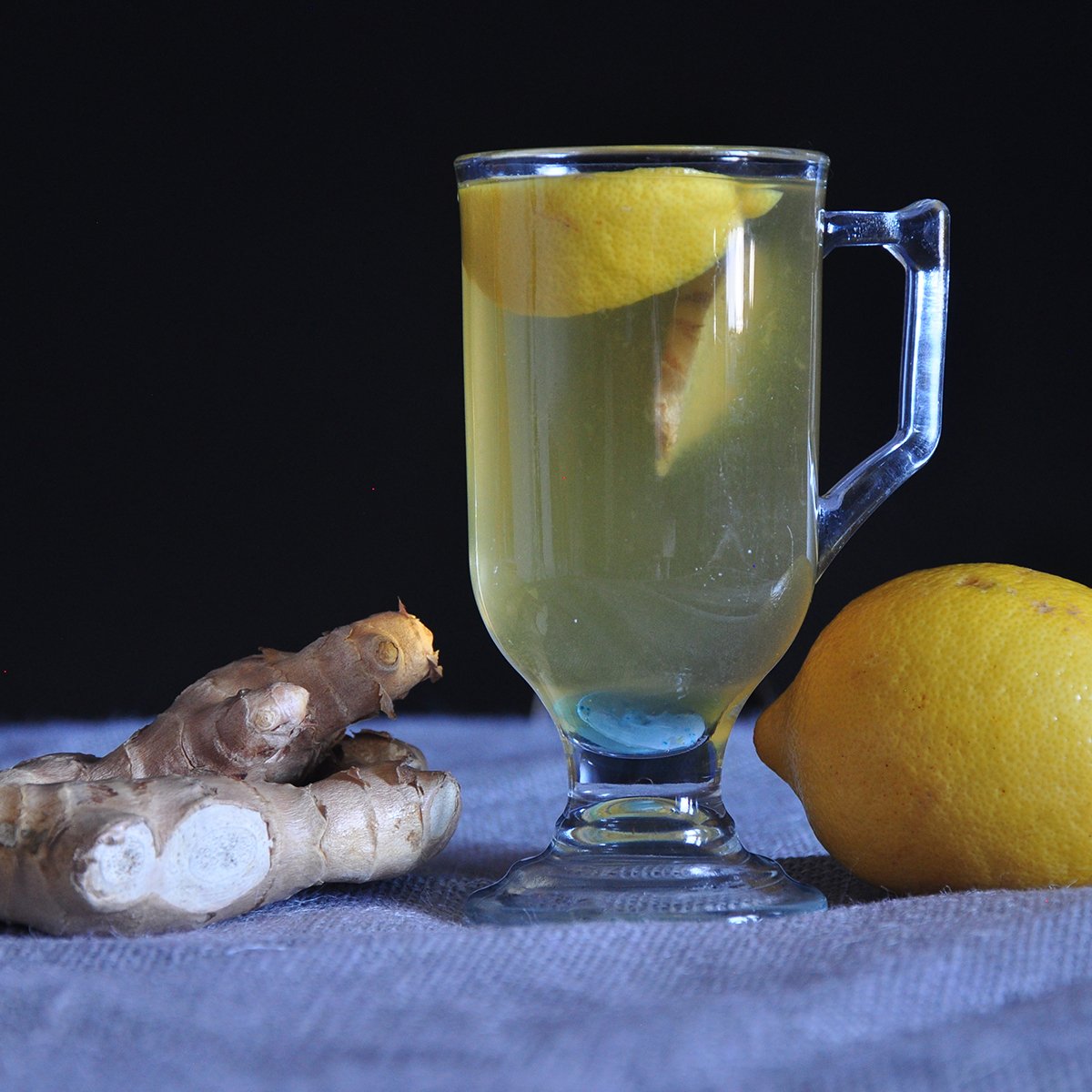 Hot toddy for a cold pictured with a lemon and ginger on a tablecloth covered counter