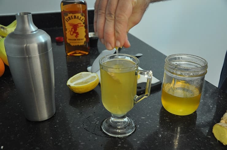 Squeezing lemon into completed 'Hot Toddy for a Cold' cocktail. Fireball, honey, and lemon in background.