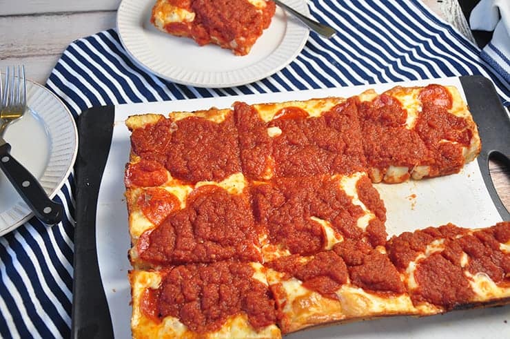 A Detroit Style Pizza on a cutting board with one piece taken out.