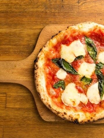 header image for pizza styles post - this is a margarita pizza on a wooden pizza peel