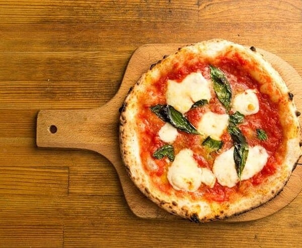 header image for pizza styles post - this is a margarita pizza on a wooden pizza peel