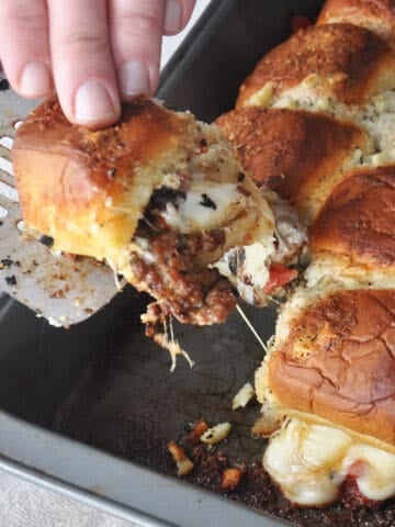 Baked pizza sliders being pulled from the oven pan
