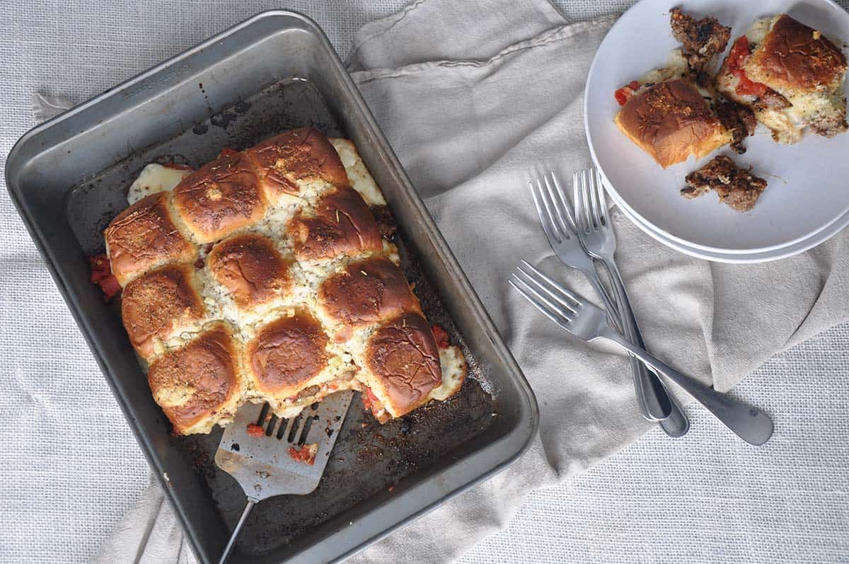 Finished Baked Pizza Sliders just waiting the be eaten and sitting in a pan next to some forks.