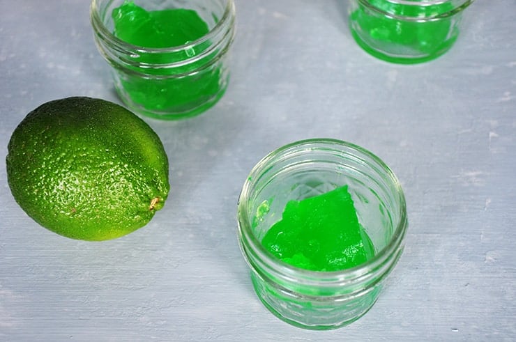 side view of two Jello shots in small mason jar with a lime.
