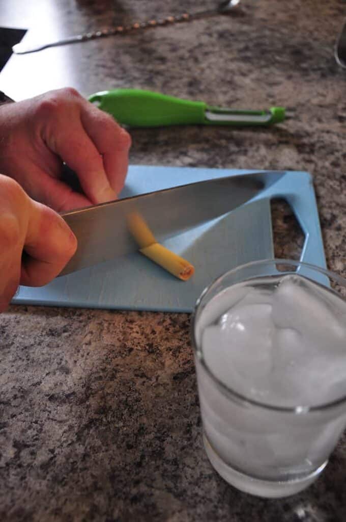 cutting lemongrass on a blue cutting board with glass of water