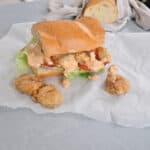 A Po' Boy sandwich on a sandwich paper with french roll in the background