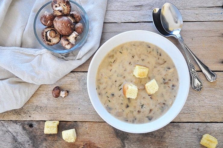 Completed cream of mushroom soup on old plankwood with sides of mushrooms and croutons.