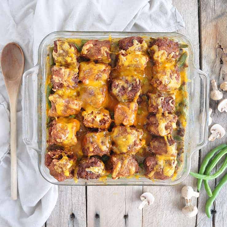 completed tater tot hotdish on some wood panels with mushrooms, green beans, and a wood spoon in the background