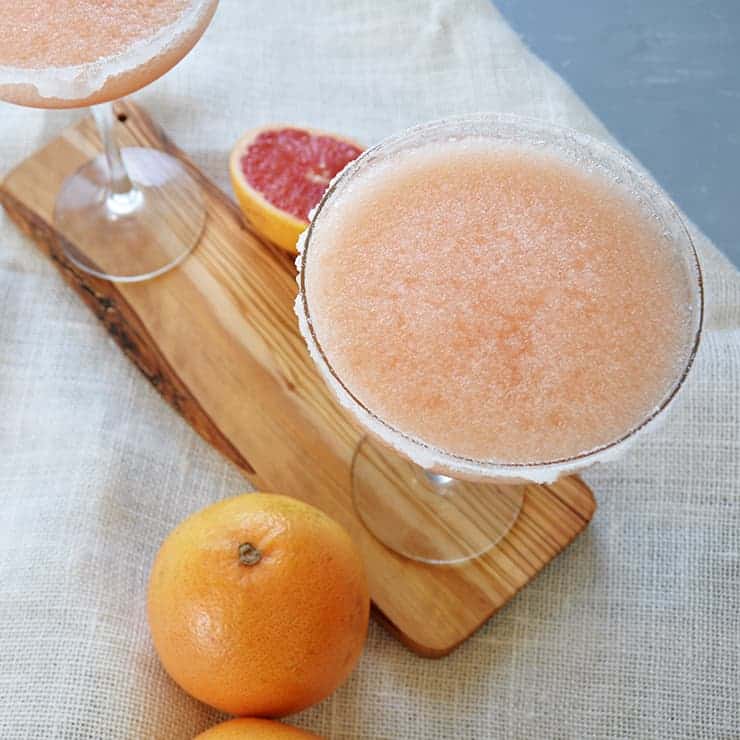 Completed Greyhound Margarita cocktail on a cutting board with a grapefruit halved and a few whole grapefruits displaying