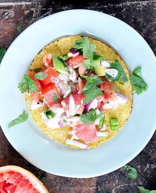 Grapefruit ceviche on a tostada that is also on a white plate with a grapefruit in the background and cilantro sprinkled on the plate