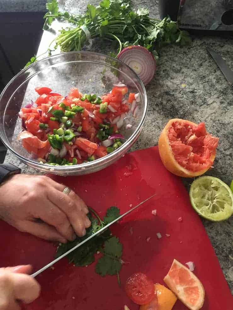 cutting cilantro on red cutting board with spent lime and grapefruit in the background, as well as a bowl of the fresh stuff