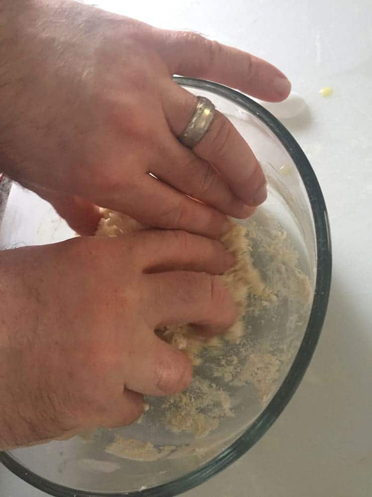 Hand in glass bowl kneading dough. 