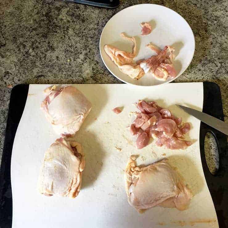 Four chicken thighs on a cutting board. One is cleaned, deboned, and chopped. The rest are whole.