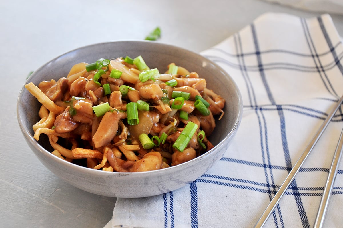 finished chow mein photograph from the side on a plaid napkin and chopsticks on the side.