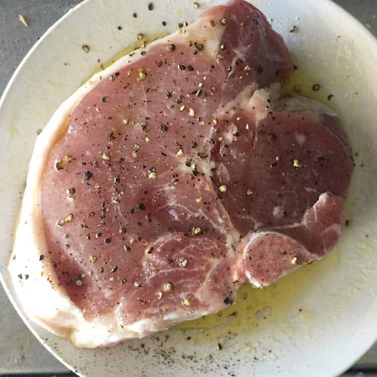 Coating raw pork chop with olive oil, salt, and pepper.