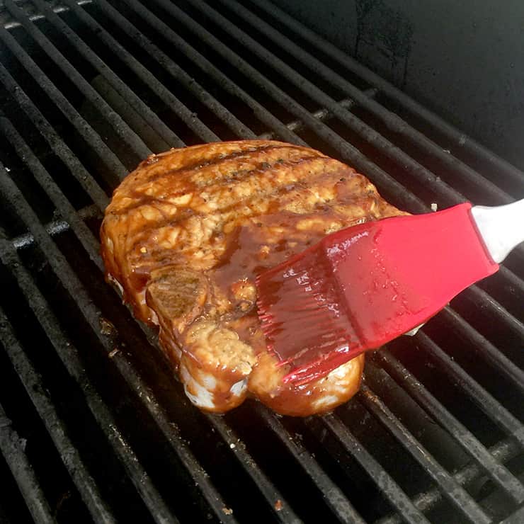 Pork Chops on the grill and I am rubbing bbq sauce on it while it is cooking.