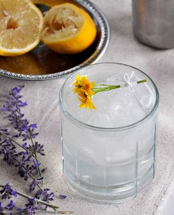 This is a Rum Daisy cocktail on a white mat with purple lavender and a few spent lemon halves in the background