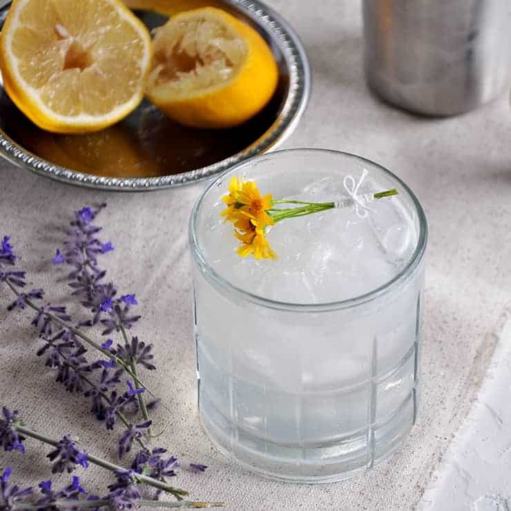 This is a Rum Daisy cocktail on a white mat with purple lavender and a few spent lemon halves in the background