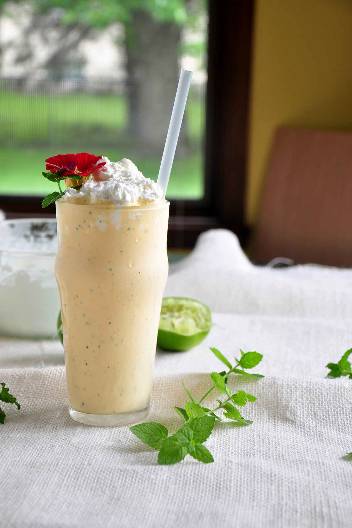 This an Ice Cream Mint Margarita and shot from the side. There is mint and lemon in the background, as well as a window.