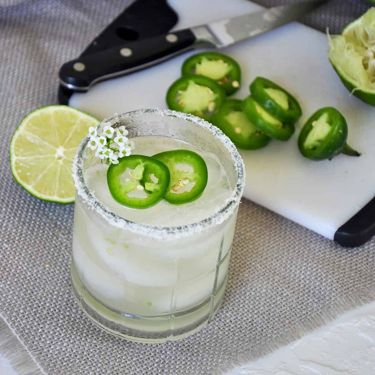 Watermelon Spicy Margarita on a white mat wihth jalepeno slices and a lime half in the background