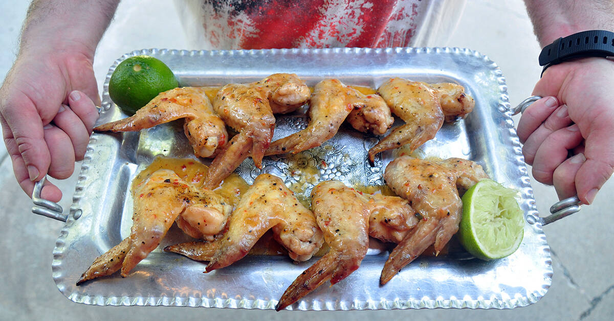 Eight full chicken wings on a silver platter being held up with two hands.