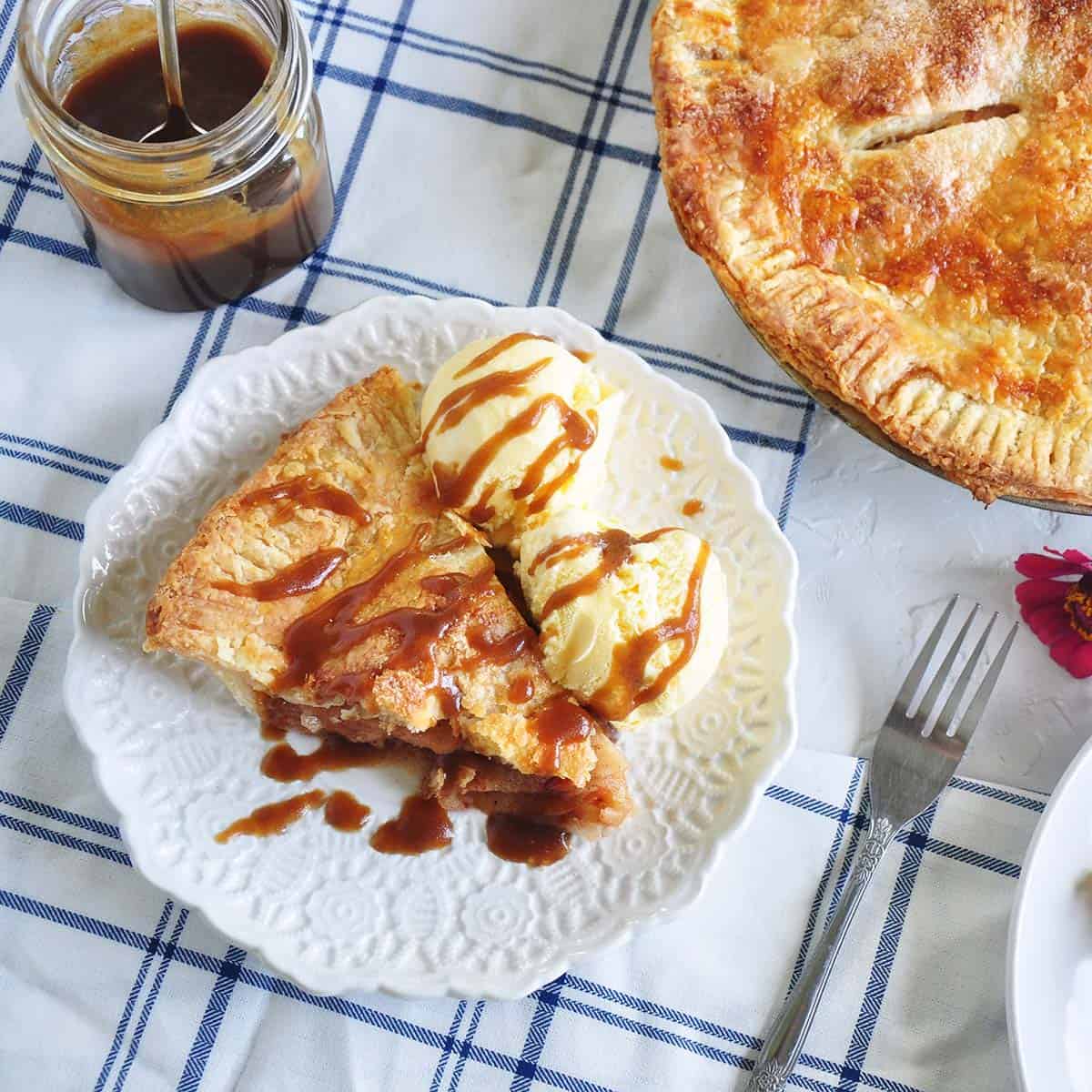 Overhead view of one slice of apple pie with two scoops of vanilla ice cream and caramel sauce in the background.