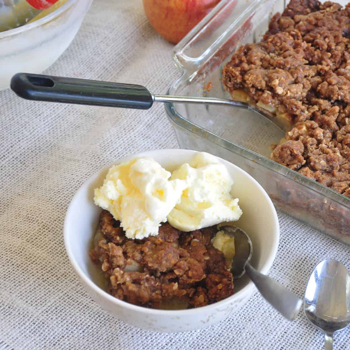 Apple Crisp in a bowl with vanilla ice cream and a tray in the background