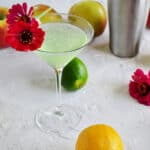 Appletini with lemons, limes, apples and flowers in the background.