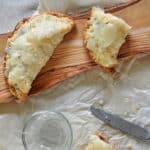 One whole Hand Pie and on that is cut in half. It is sitting on a rustic wooden cutting board and on top of some parchment paper