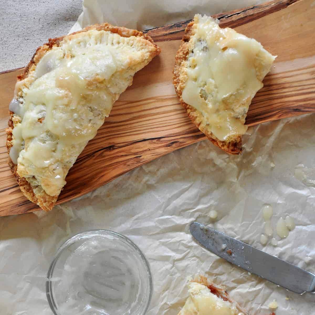 One whole Hand Pie and on that is cut in half. It is sitting on a rustic wooden cutting board and on top of some parchment paper.