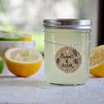 Jar of Homemade Sweet and Sour Mix with two lemons and some limes showing in the background