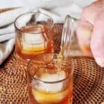 One full glass of apple brandy and one being poured into a glass placed on a wicker basket.
