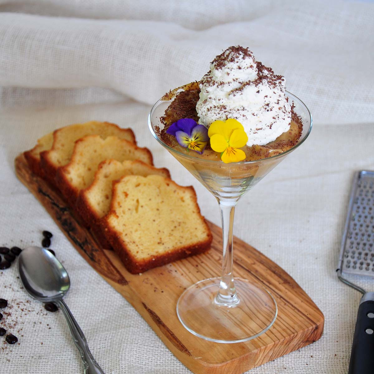 White Russian Mini Trifle on a cutting board with 4 pieces of vanilla bread. It is on a white cloth with a spoon and a grater.