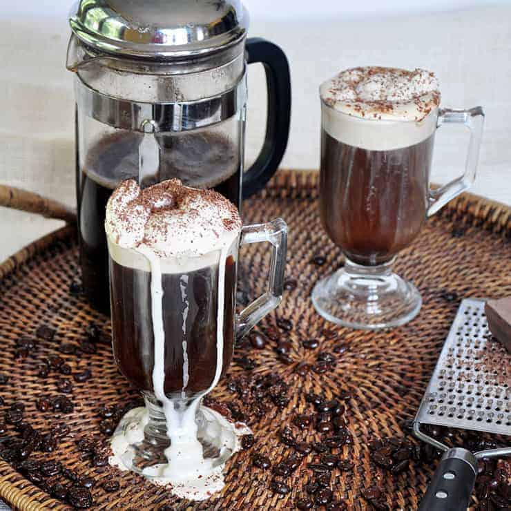 Two Glasses of Russian Coffee with a french press in the background and ornamental coffee beans all over the place.