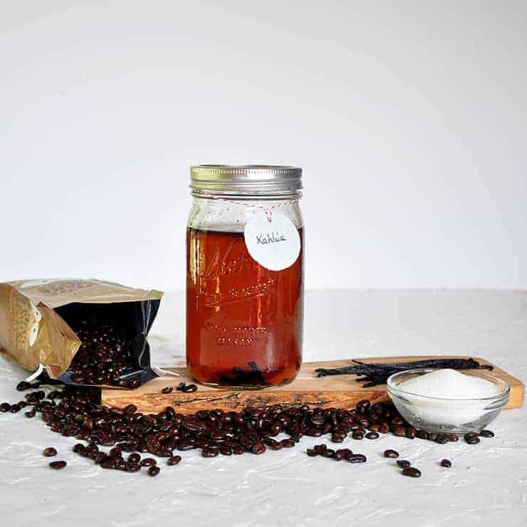 This is a quart of DIY kahlua on a wood platform with sugar and coffee beans on the platform.