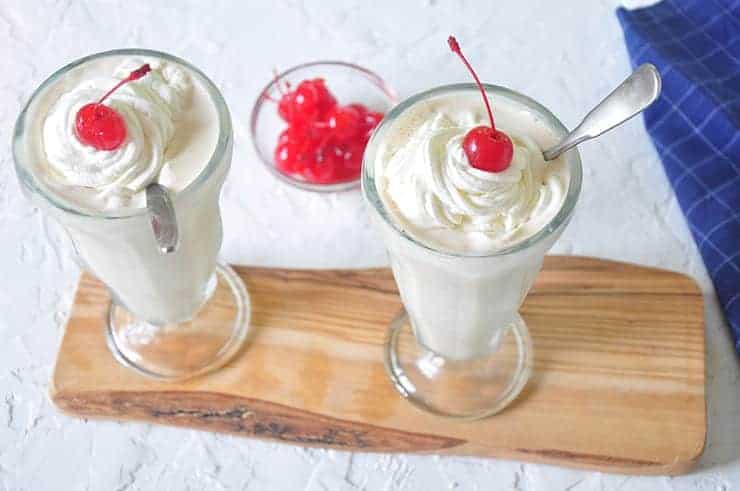 White Russian Alcoholic Milkshakes on a wood cutting board with some cherries in the background.