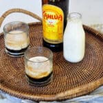 Two Classic White Russian cocktails on a platter with a container of milk and a bottle of Kahlua