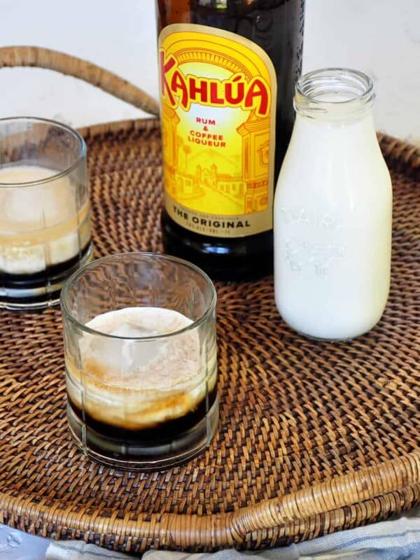 Two Classic White Russian cocktails on a platter with a container of milk and a bottle of Kahlua