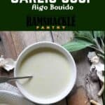 "Julia Child's Garlic Soup - Aigo Bouido" with a bowl of soup on wood with sage and garlic in the background.