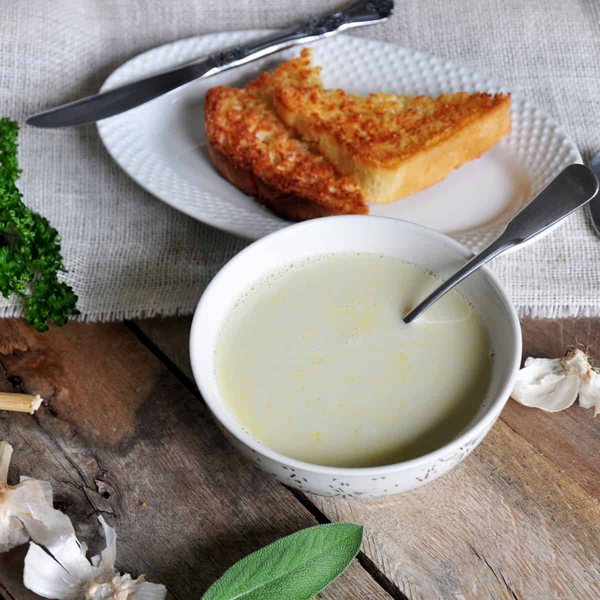 Aigo Bouido Recipe in a bowl on a picnic table. There is toasted bread on the side with herbs showing.