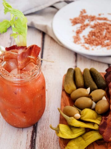 Bacon Bloody Mary with a tray of pickles and olives. In the background is the bacon salt that is used on the drink