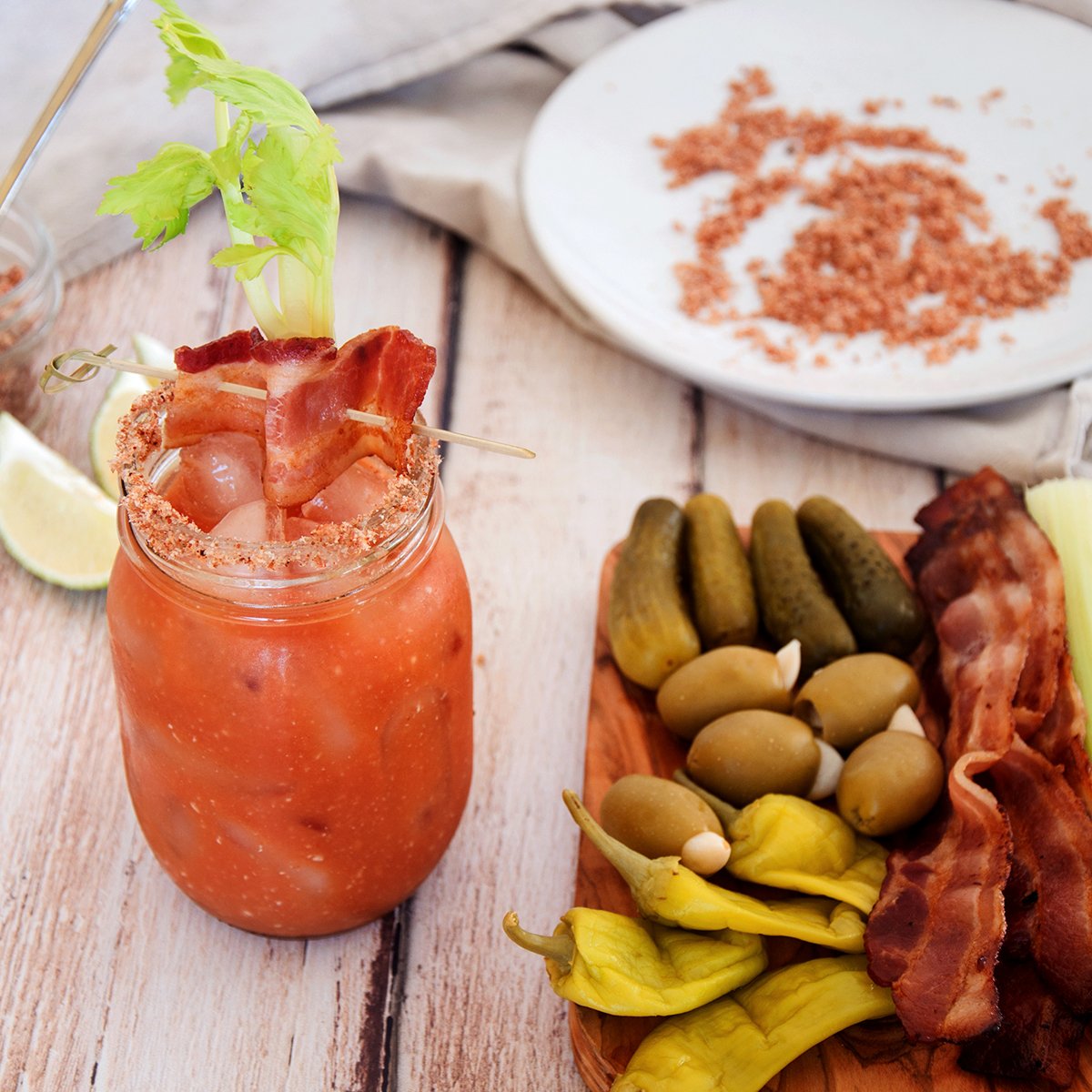 Bacon Bloody Mary with a tray of pickles and olives. In the background is the bacon salt that is used on the drink.